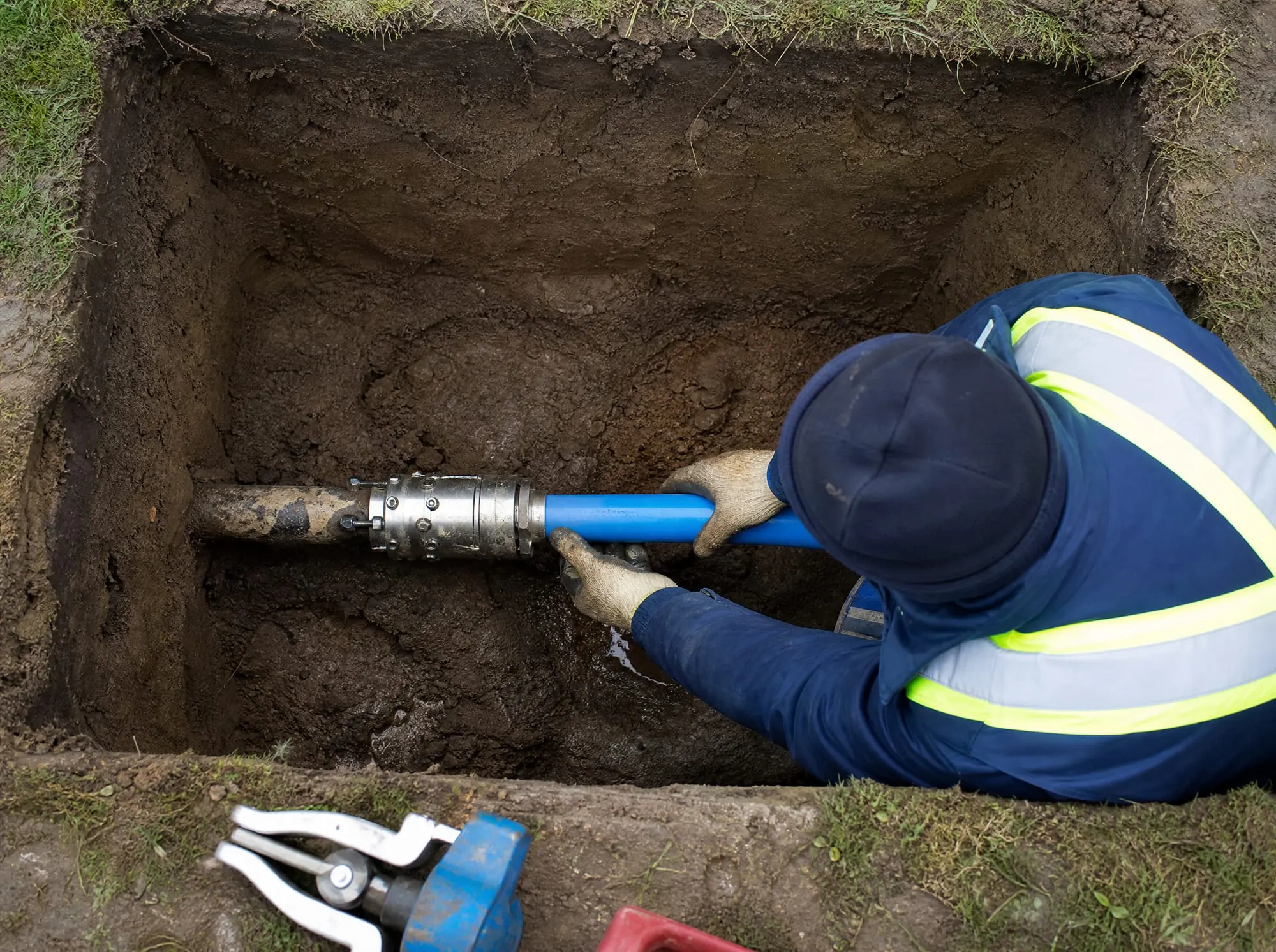 Illustrative photo of a small access pit on a front lawn with a new blue water pipe being pulled through