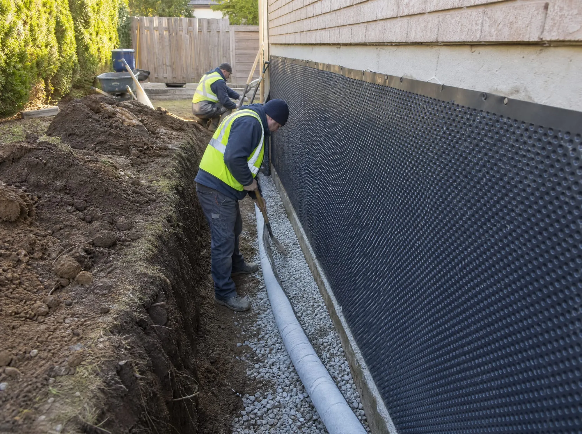 Illustrative photo of an excavated foundation with drainage membrane and a new weeping tile pipe on clear stone